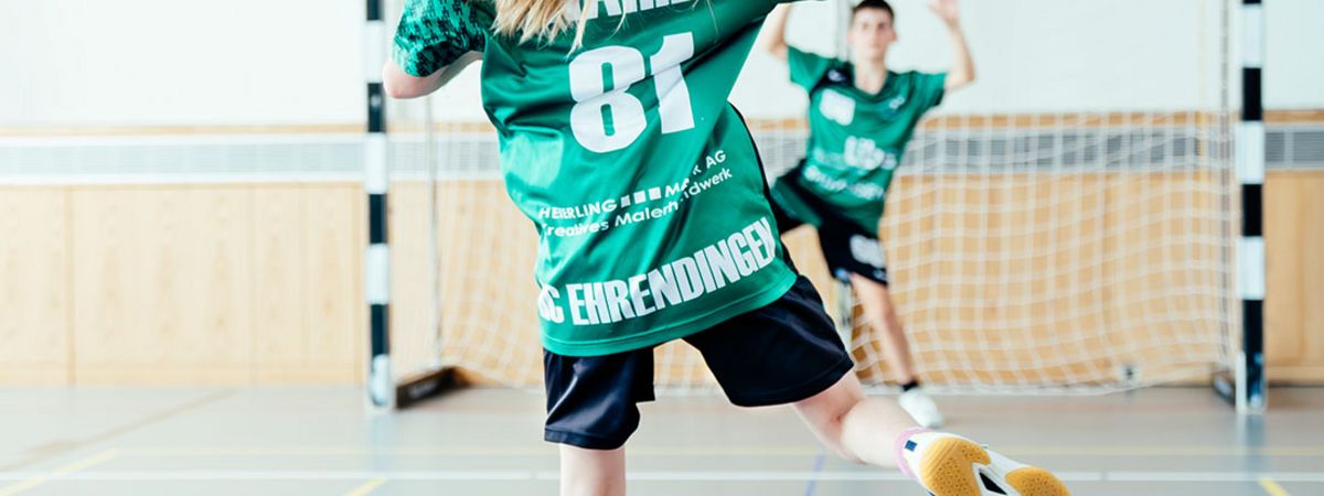 Blondes Mädchen von hinten im Ehrendinger Vereinsdress beim Torschuss im Handball in der Turnhalle Ehrendingen